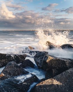 Waves splashing on rocks at shore against sky