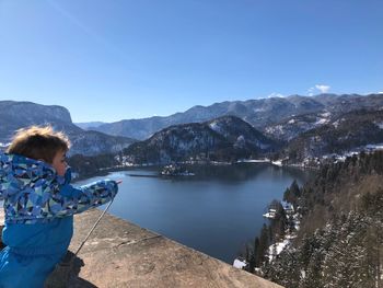 Side view of boy pointing by lake against sky during winter