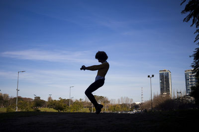 Side view of woman dancing on land against blue sky