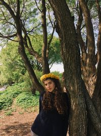 Portrait of woman wearing wreath while leaning on tree outdoors