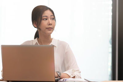 Smiling businesswoman using laptop while looking away in office