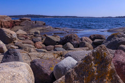 Rocks by sea against clear blue sky