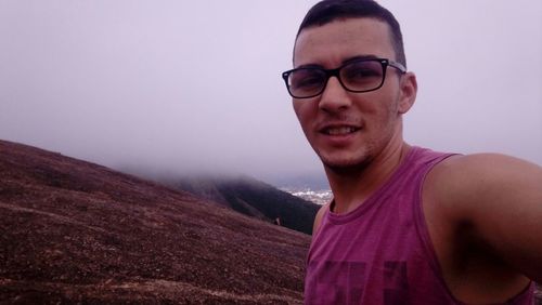 Young man wearing sunglasses standing on mountain against sky