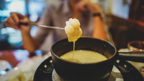Midsection of person holding fork over bowl with cheese fondue at home