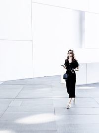 Full length portrait of young woman standing against tiled wall