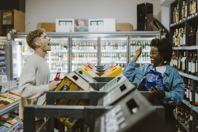 Happy woman throwing chips in boyfriend's mouth while doing shopping at supermarket