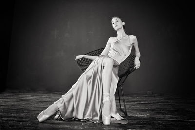 Portrait of a ballerina in a pink dress is sitting on a chair with her leg in the slit of the dress
