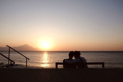 Couple sitting on shore against sky during sunset