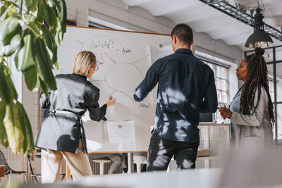 Businesswoman planning strategy on white board while standing with male and female colleagues at office