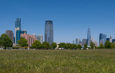 Scenic view of field by modern buildings against clear sky