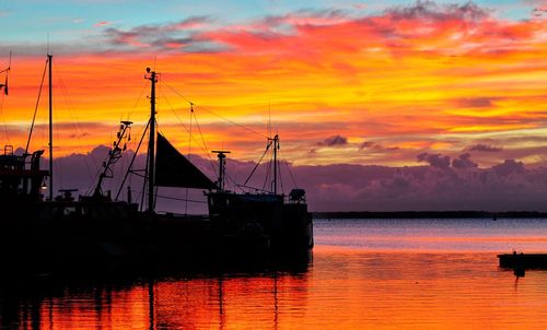 Silhouette sailboat on sea against orange sky