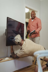 Male technician repairing television while talking with man at home