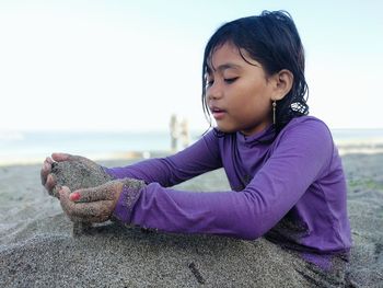 Girl sitting on shore at beach against sky