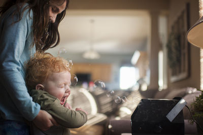 Playful sister carrying brother by bubble blowing machine while playing at home