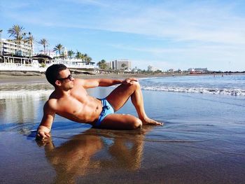 Shirtless mid adult man relaxing at beach against sky