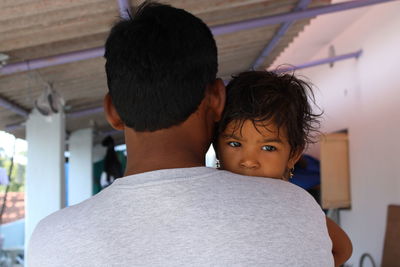 Rear view of father carrying daughter while standing in house