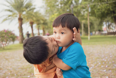 Close-up of boy kissing sister while standing against trees in park