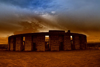 Silhouette of built structure on field against cloudy sky