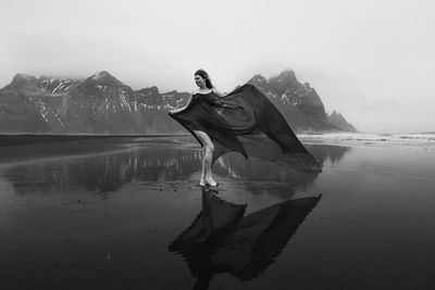 Lady in waving chiffon dress on empty beach monochrome scenic photography