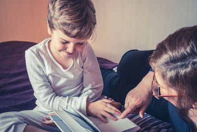 Grandmother reading book for grandson on bed