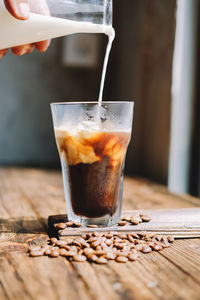 Cropped hand pouring milk in iced coffee on wooden table