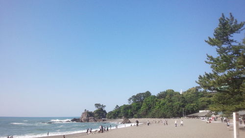 People on beach against clear blue sky