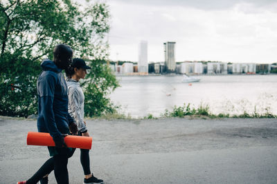 Male athlete holding yoga mat while walking with female friend on road in city