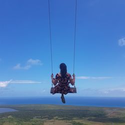 Rear view of woman sitting on swing against sky