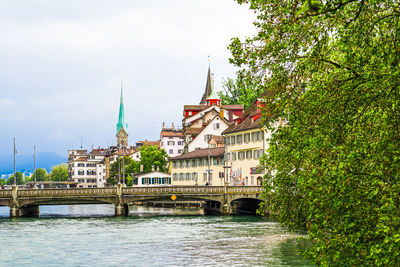 Bridge over river by buildings in city against sky