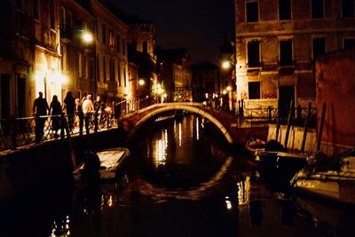 Bridge over canal amidst buildings in city at night