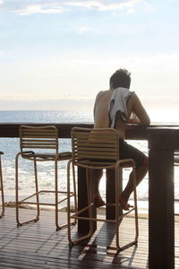 Rear view of man sitting on chair at beach