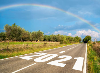 Road by trees against rainbow in sky