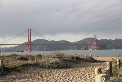 Suspension bridge over sea against cloudy sky