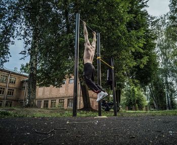 Full length of shirtless man exercising by trees on rod