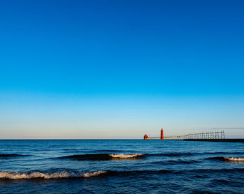 Morning light illuminates the lighthouse and pier against a clear blue sky at grand haven, michigan