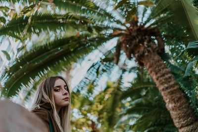 Portrait of young woman standing by palm tree