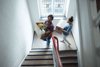 Smiling man and woman with cardboard boxes moving up on staircase