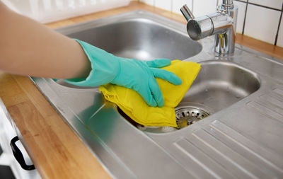 Midsection of person with faucet in kitchen at home