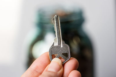 Close-up of hand holding key against white background, coin jar