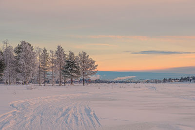 Snow covered field against sky during sunset