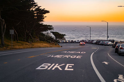 Road by sea against sky during sunset