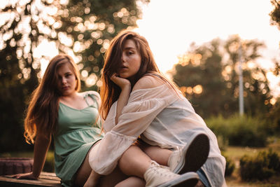 Portrait of lesbian couple sitting on bench in park in summer