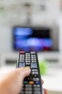 Cropped hand of woman watching tv at home