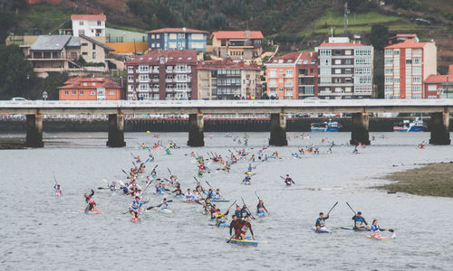 People canoeing on river against buildings