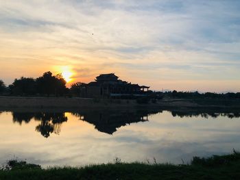 Scenic view of lake by building against sky at sunset