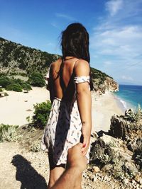Rear view of woman standing at beach against sky