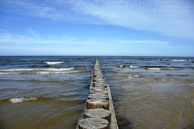 Wooden posts in sea against sky