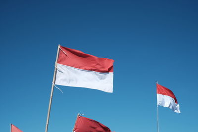Low angle view of indonesian flags against clear blue sky