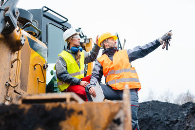 People working on construction vehicle against sky