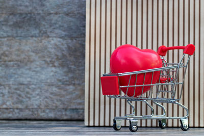 Close-up of red heart shape in shopping cart against wall